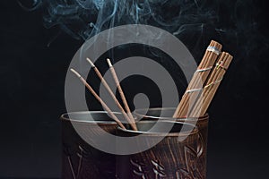 Burning incense sticks and brown bowl on black background. Beautiful smoke from above
