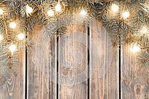 Burning lit light bulbs of Christmas tree branches garland lying on plank surface. Rustic holiday background, copy space