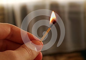 A burning match in the hand of a teenager. A match with a flame of fire on a dark background.