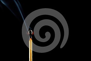 A burning match with smoke on a black background. Space for text.