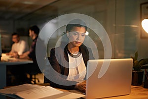 Burning the midnight oil. Shot of a young businesswoman using her laptop while working overtime in the office.