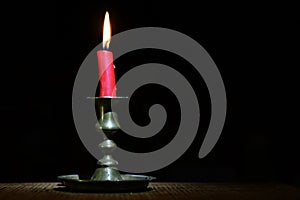 Burning old candle vintage bronze candlestick on black wooden background.