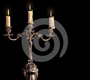 Burning old candle vintage bronze Silver candlestick. Isolated Black Background.