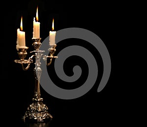 Burning old candle vintage Silver bronze candlestick. Isolated Black Background.