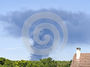 A Burning plastic recycling place causes a big pile of dark, black thick smoke on a sky blue summer day. Danger, sorrow. Terrorist