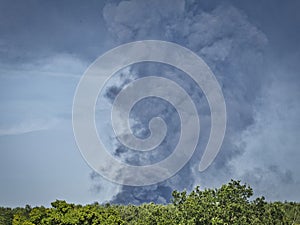 A Burning plastic recycling place causes a big pile of dark, black thick smoke on a sky blue summer day. Danger, sorrow. Terrorist