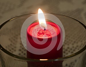 Burning red candle in a glass holder, close up