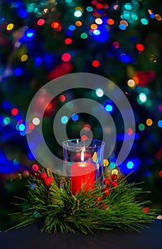 A burning red candle in the middle of the Christmas wreath against the dark background on the christmas tree