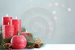 Burning red candles with Christmas decor on table against blurred lights