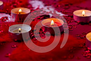 Burning red candles on confetti sequinned background with feathers. Saint Valentines Day and Christmas background . Holidays