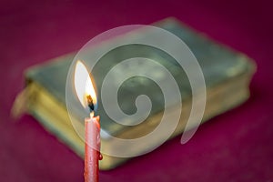 Burning red church candle and blurred holy bible behind