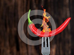 burning red hot chili pepper on a fork on dark wooden background, concept of cooking or eating hot and spicy food