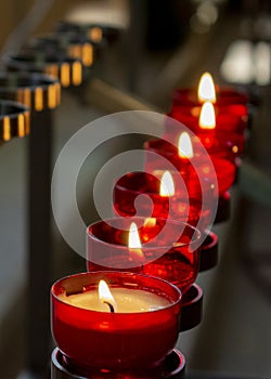 Burning red prayer candles inside a catholic church on a candle rack. Selective focus