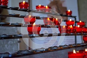 Burning red prayer candles inside a catholic church on a candle rack. Selective focus