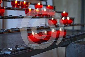 Burning red prayer candles inside a catholic church on a candle rack. Selective focus