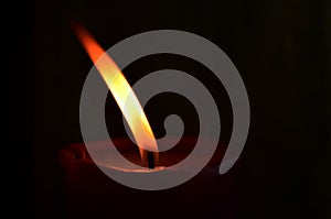 Burning single red candle with dancing flame on the dark background