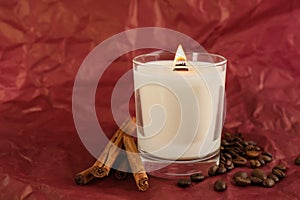 Burning soy candle, cinnamon sticks and coffee beans on crumpled red paper, space for text