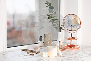 Burning soy candles, cosmetics and stylish accessories on white window sill indoors