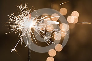 Burning sparkler stands in a glass. Dark background with defocused multi-colored lights of garland.