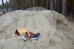 Burning sports sneakers or gym shoes on fire stand on sandy beach coast. Athlete burned out. Physical exertion during training