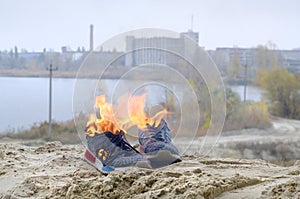 Burning sports sneakers or gym shoes on fire stand on sandy beach coast. Athlete burned out. Physical exertion during training