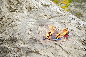 Burning sports sneakers or gym shoes on fire stand on sandy beach coast. Athlete burned out. Physical exertion during training