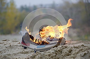 Burning sports sneakers or gym shoes on fire stand on sandy beach coast. Athlete burned out. Physical exertion during training