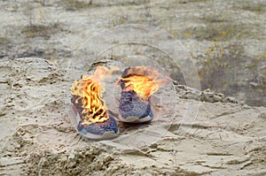 Burning sports sneakers or gym shoes on fire stand on sandy beach coast. Athlete burned out. Physical exertion during training