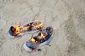 Burning sports sneakers or gym shoes on fire stand on sandy beach coast. Athlete burned out. Physical exertion during training