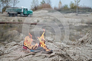 Burning sports sneakers or gym shoes on fire stand on sandy beach coast. Athlete burned out. Physical exertion during training