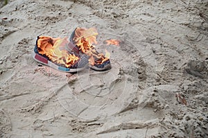 Burning sports sneakers or gym shoes on fire stand on sandy beach coast. Athlete burned out. Physical exertion during training