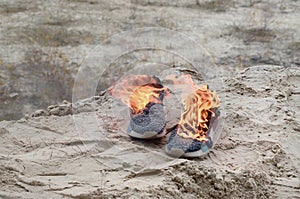 Burning sports sneakers or gym shoes on fire stand on sandy beach coast. Athlete burned out. Physical exertion during training