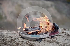 Burning sports sneakers or gym shoes on fire stand on sandy beach coast. Athlete burned out. Physical exertion during training