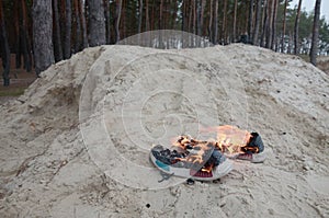 Burning sports sneakers or gym shoes on fire stand on sandy beach coast. Athlete burned out. Physical exertion during training