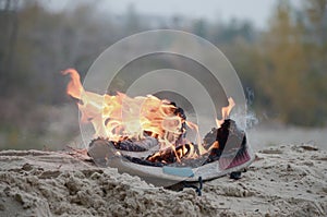 Burning sports sneakers or gym shoes on fire stand on sandy beach coast. Athlete burned out. Physical exertion during training