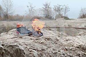 Burning sports sneakers or gym shoes on fire stand on sandy beach coast. Athlete burned out. Physical exertion during training