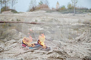 Burning sports sneakers or gym shoes on fire stand on sandy beach coast. Athlete burned out. Physical exertion during training