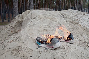 Burning sports sneakers or gym shoes on fire stand on sandy beach coast. Athlete burned out. Physical exertion during training