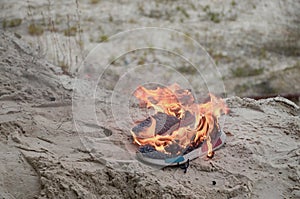 Burning sports sneakers or gym shoes on fire stand on sandy beach coast. Athlete burned out. Physical exertion during training