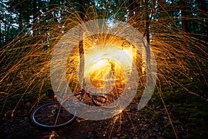 Burning steel wool spinned in the forest with a bicycle in the foreground . Showers of glowing sparks from spinning steel wool