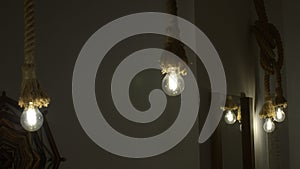 Burning stylish light bulbs decorated by ropes. Media. Stylish hanging bulbs, ethnic interior.