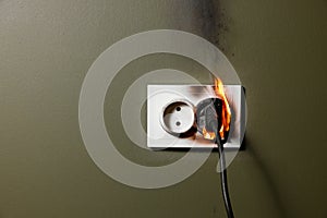 burning wall electrical socket with plugged appliance cable from short circuit in house. concept of fire safety and power overload
