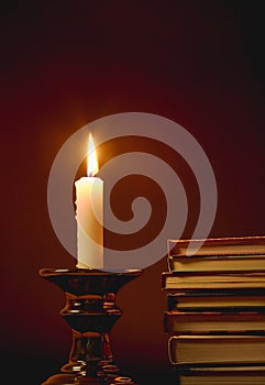 Burning white candle and ancient books on retro candlestick on dark night background