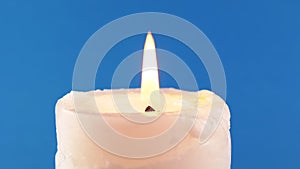 Burning White Candle with a Bright Flame on an Isolated Blue Background. Zoom