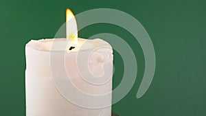 Burning White Candle with a Bright Flame on an Isolated Green Background. 4K