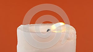 Burning White Candle with a Bright Flame on an Isolated Orange Background. Zoom