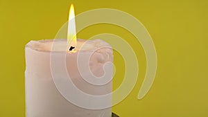 Burning White Candle with a Bright Flame on an Isolated Yellow Background. 4K