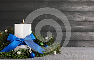 Burning white candle with Christmas decor on table against dark background. Space for text