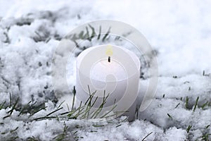 Burning white candle on snow covered coniferous branches