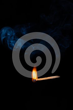 Burning wooden match with blue smoke over black background. Copy space